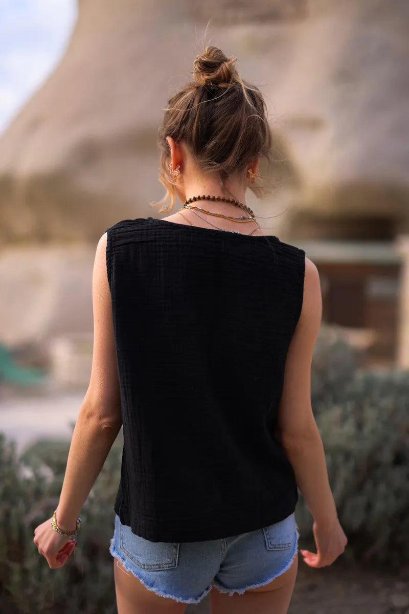 Woman wearing a black sleeveless round neck muslin cotton blouse and denim shorts walking outdoors.