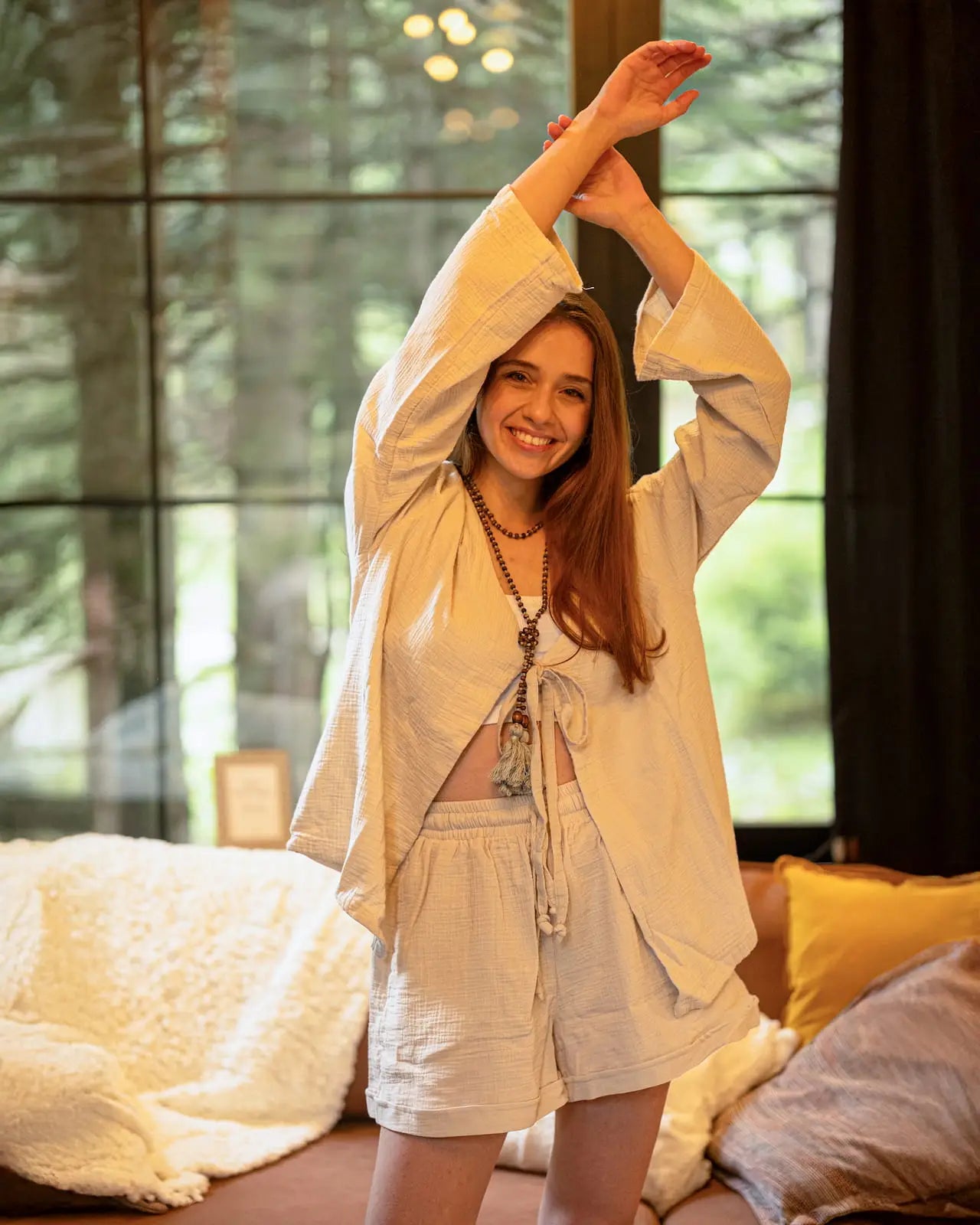 Woman in a loungewear set wit shorts  stretching in a room with large windows and soft lighting.