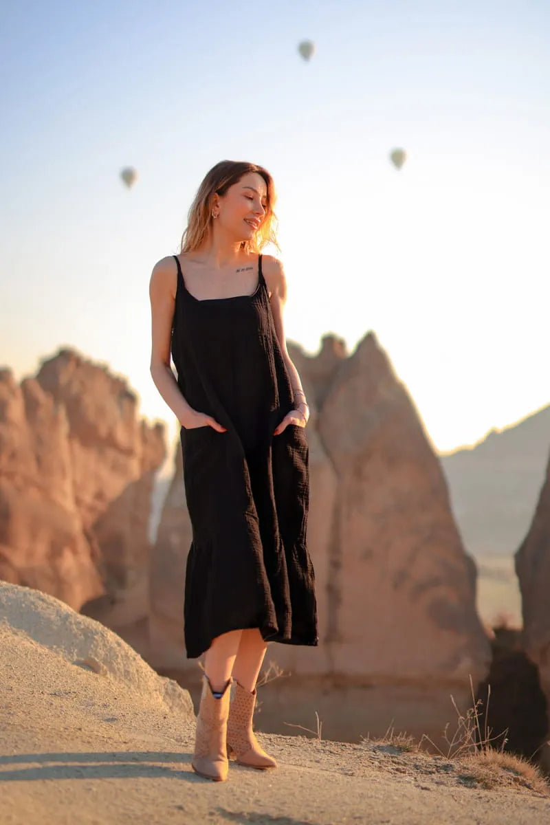 Woman in a black double gauze dress standing in a scenic landscape with balloons in the background