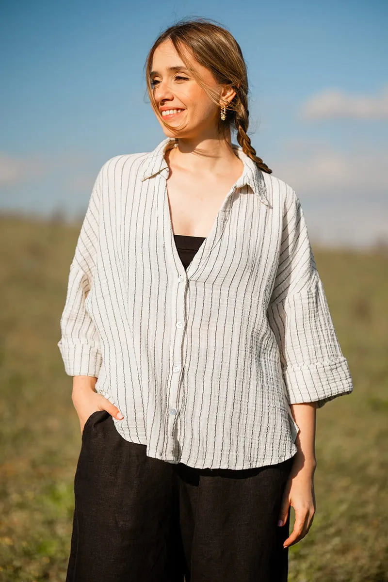 Woman wearing a striped shirt and black pants standing in an outdoor setting with a blue sky.
