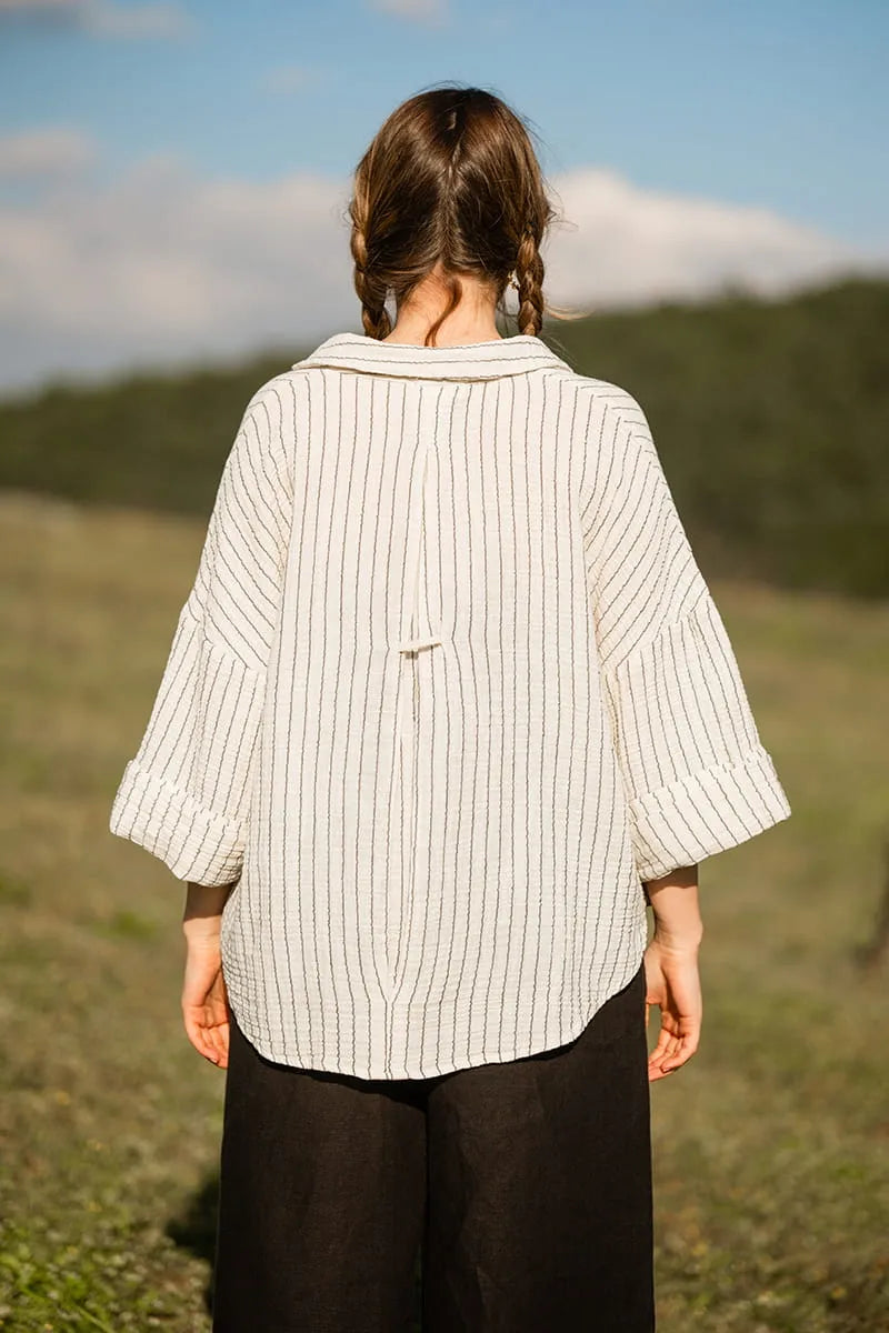 Person wearing a white striped shirt standing in a field with a scenic background