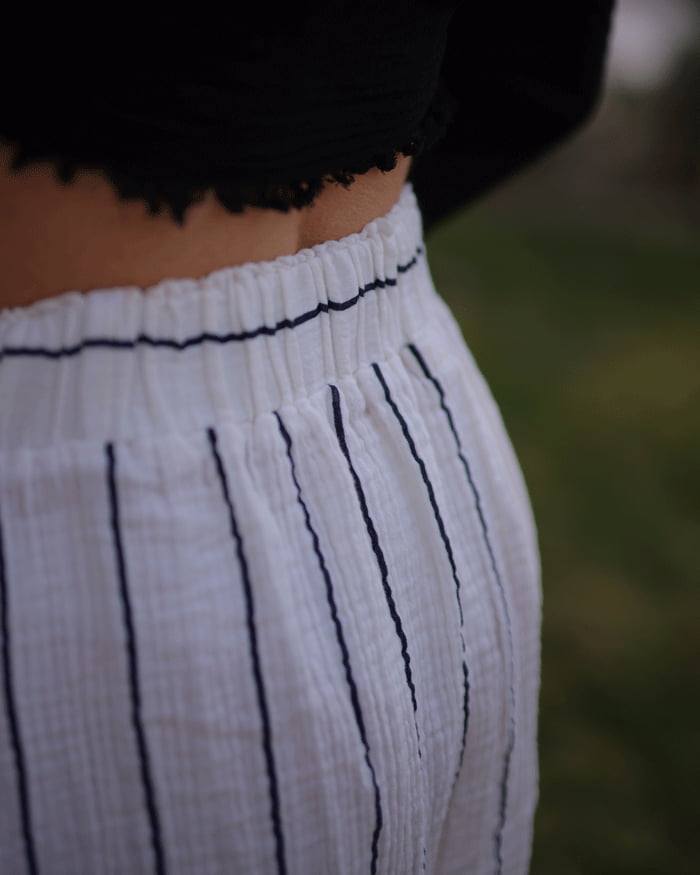 Close-up of a person wearing white pants with black stripes against a blurred natural background