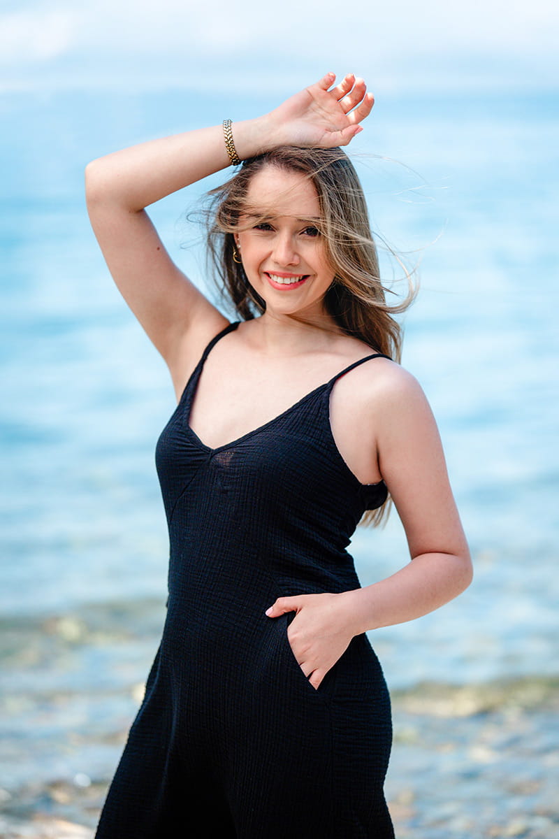 Woman in a black Maxi Slip Dresss tanding by a body of water with a blurred background