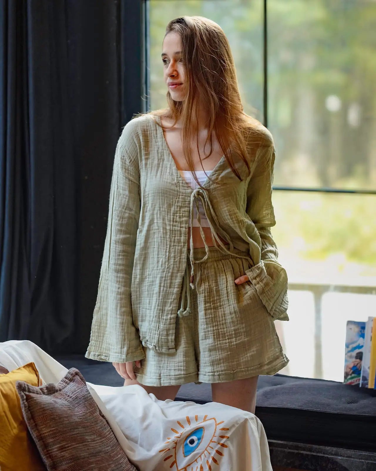 Woman in a green Loungewear Set standing by a window with a blurred outdoor view.