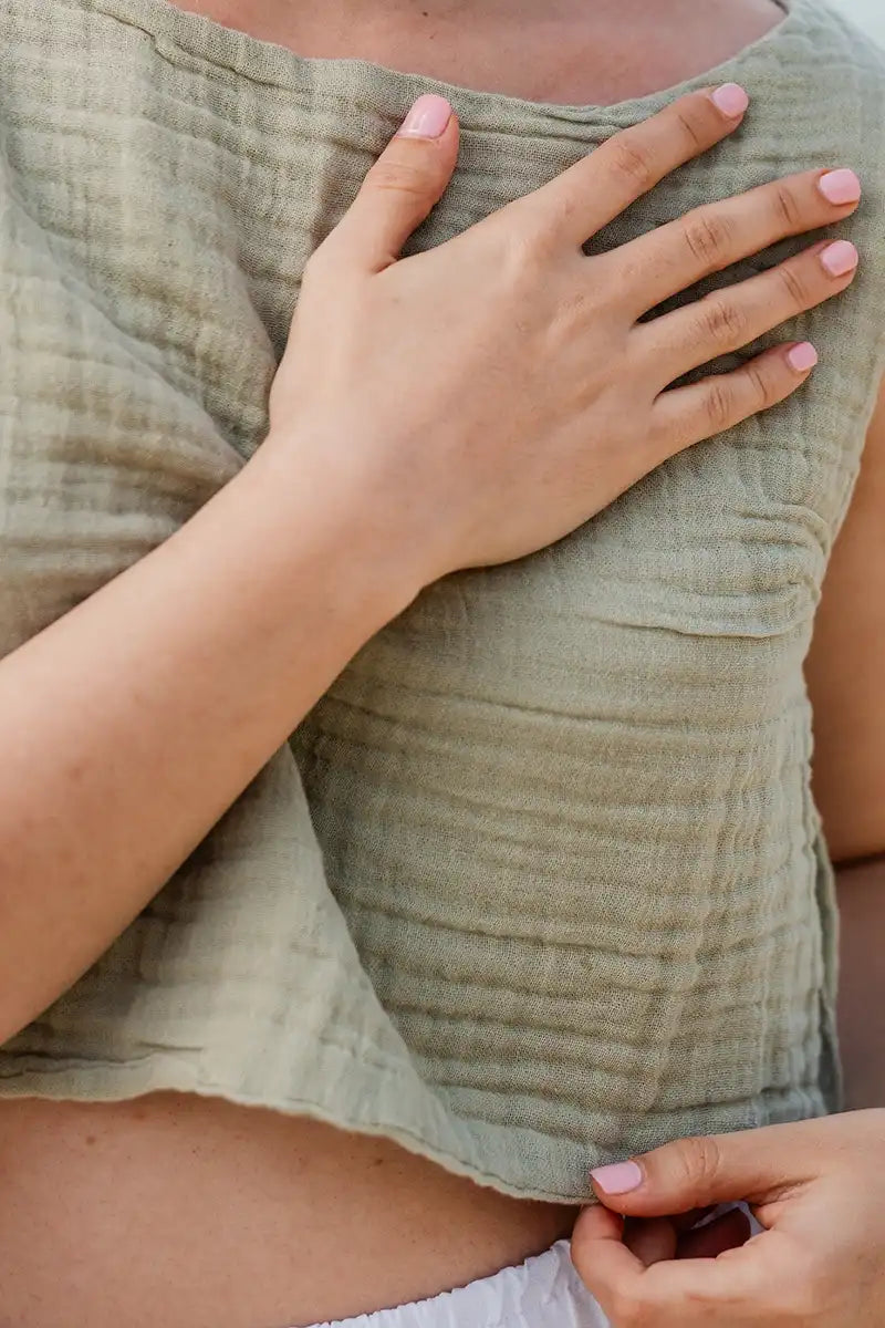 Close-up of a person wearing a cotton crinke green top with a hand on their chest.
