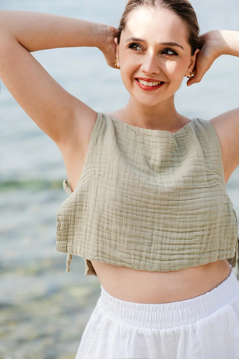 Woman wearing a light green sleeveless top and white pants with a blurred natural background