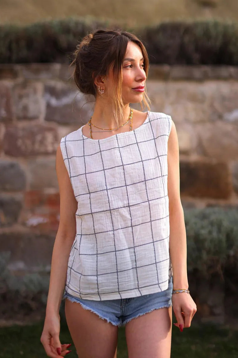 Woman wearing a sleeveless checkered top and denim shorts standing against a stone wall.