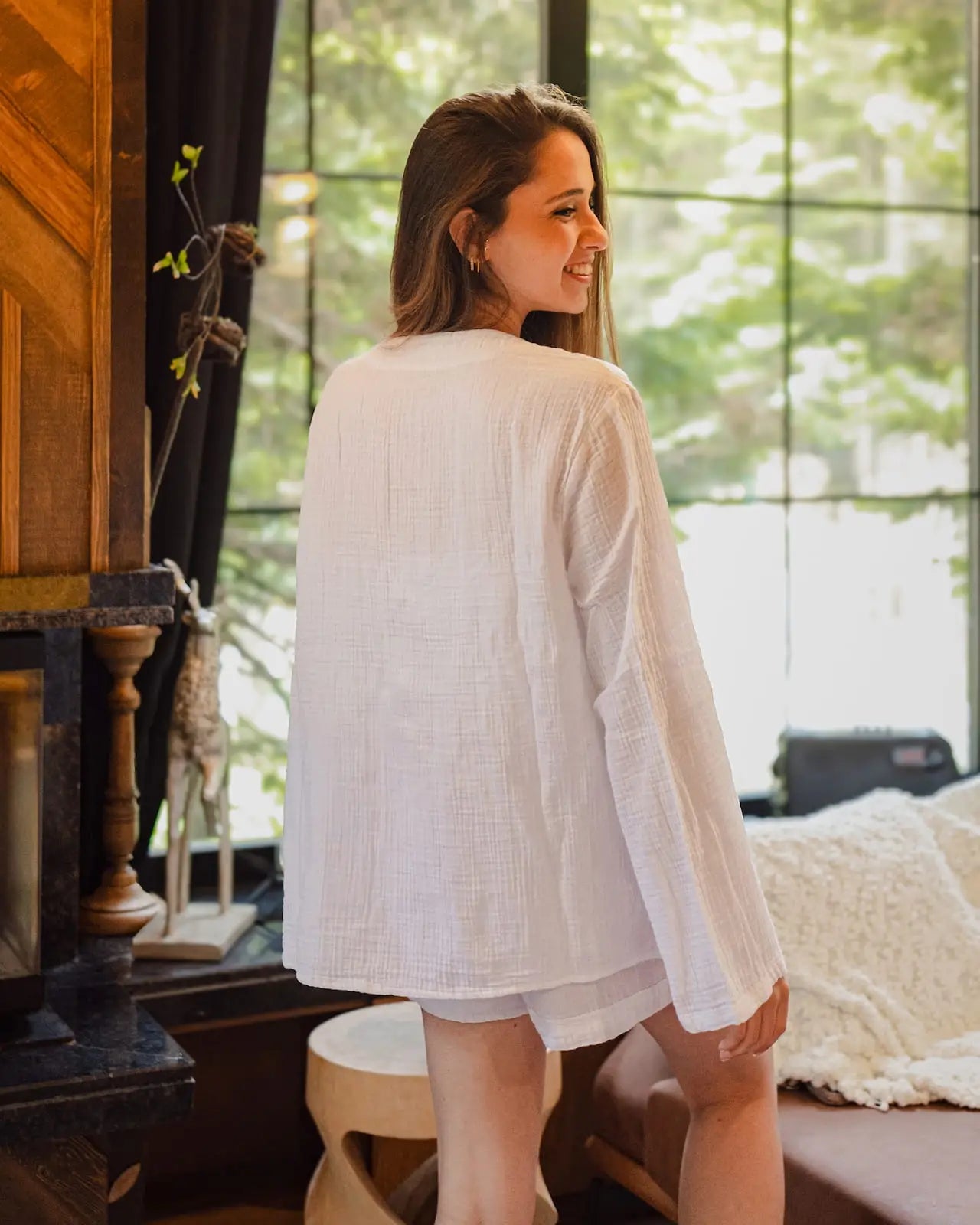 Woman wearing a white long-sleeve Pyjama top in a room with large windows.