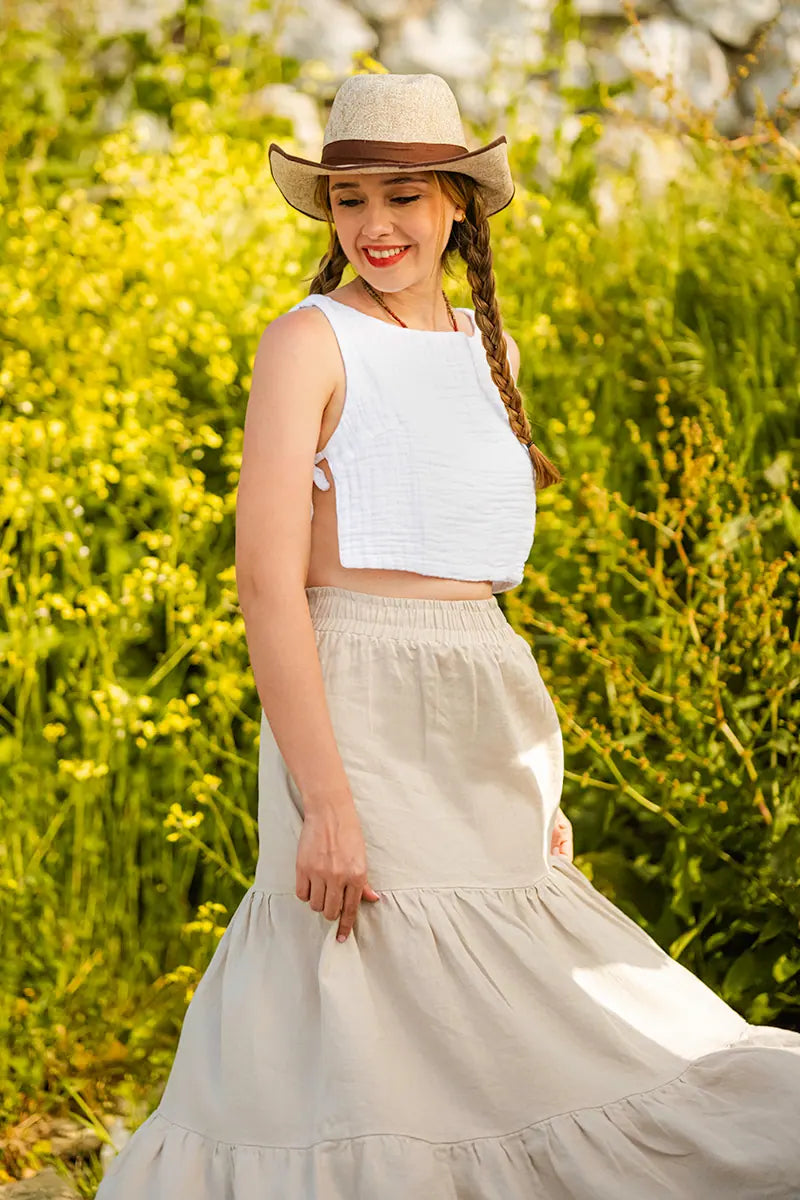 Woman in a white top and light skirt standing in a field with yellow flowers and blurred background