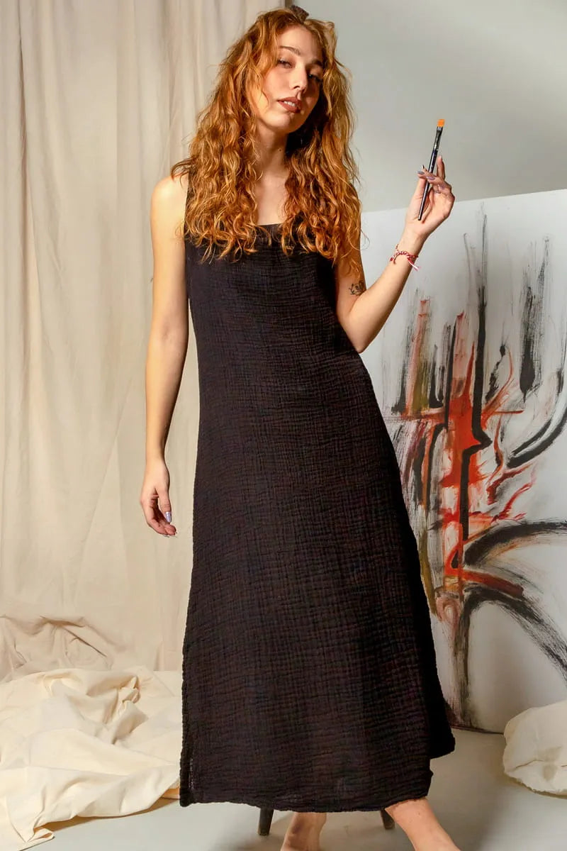 Woman in a black maxi cami dress holding a makeup brush against an abstract painting.