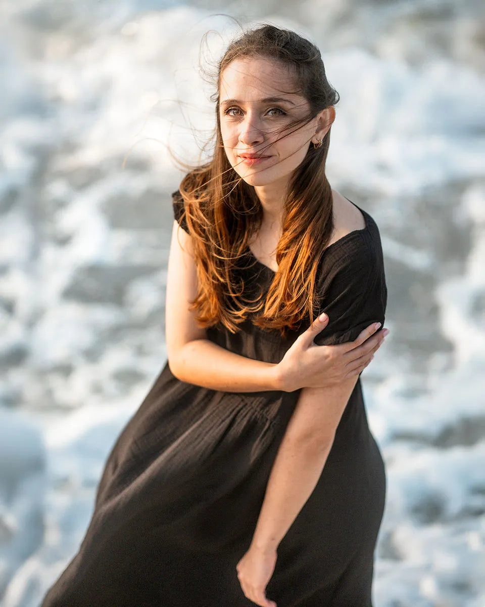 Woman in a black crinkle cotton dress standing against a blurred natural background
