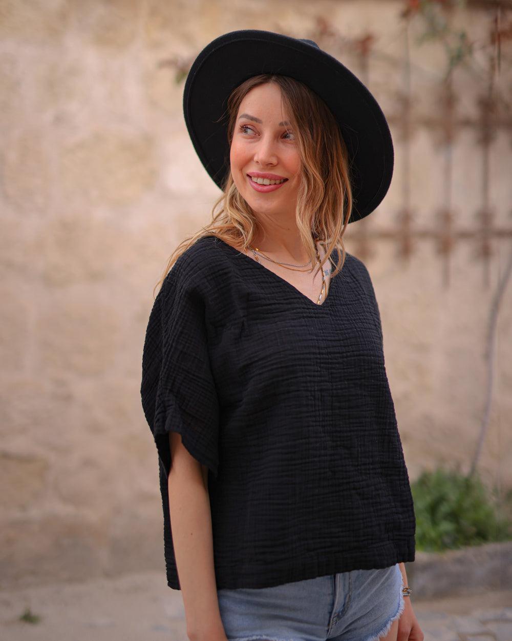A woman wearing a black v-neck t-shirt with short sleeves, paired with a wide-brimmed hat and blue denim shorts.
