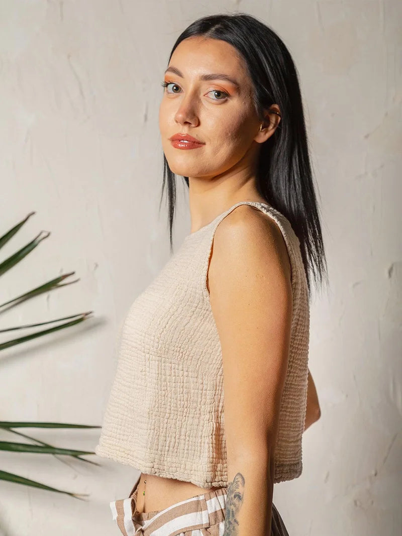 Woman wearing a beige sleeveless muslin top against a neutral background