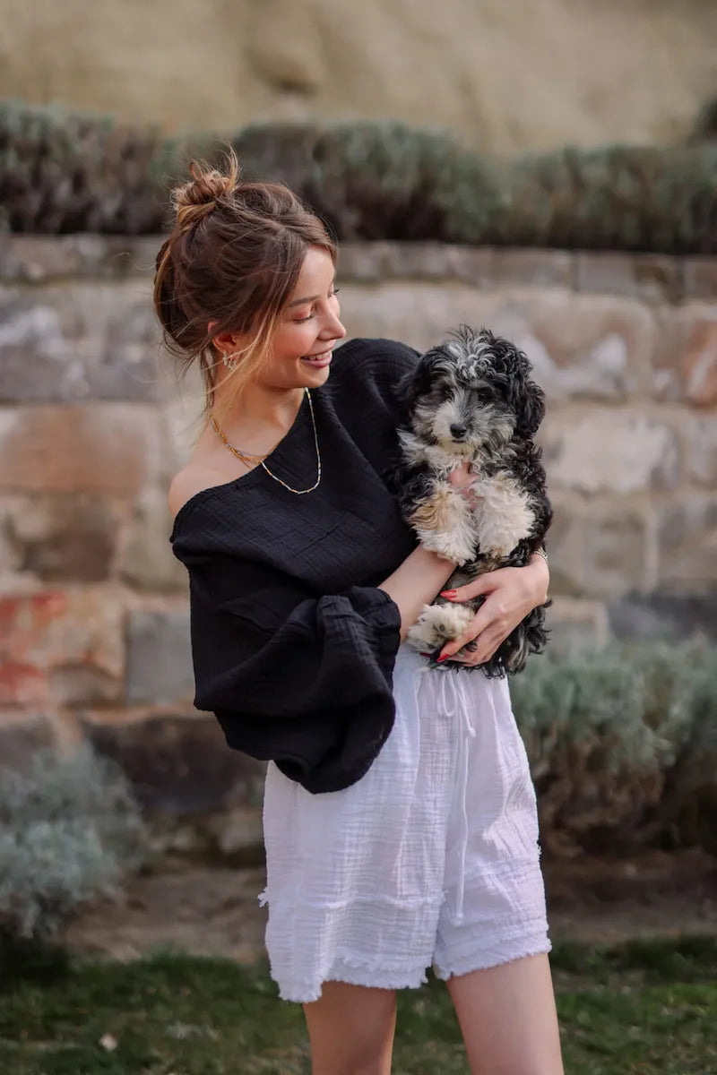 Woman holding a small dog outdoors with a stone wall and plants in the background