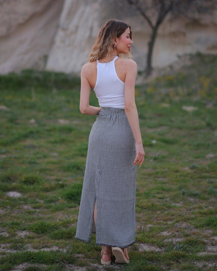 A woman standing in a field wearing a white sleeveless top and a long gauze pencil skirt.