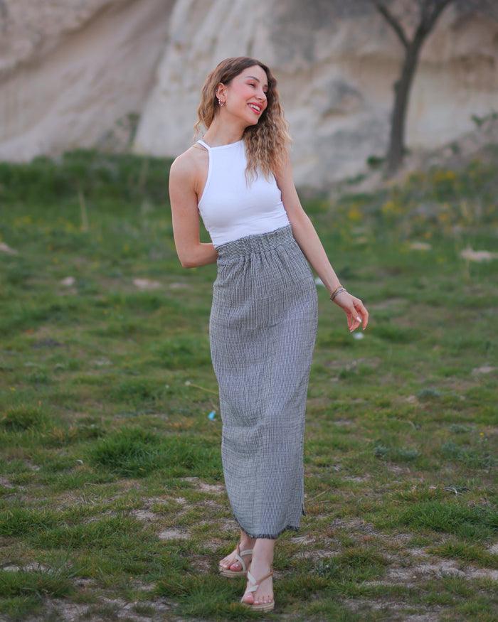 A woman standing in a field wearing a white sleeveless top and a long gauze maxi skirt.