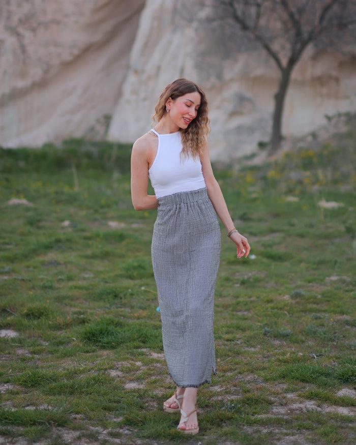A woman standing in a field wearing a white sleeveless top and a long gauze  cotton maxi skirt.