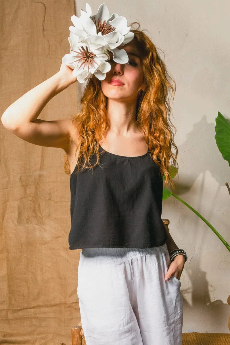 Woman wearing a black open neck linen top and white pants, holding a large white flower.