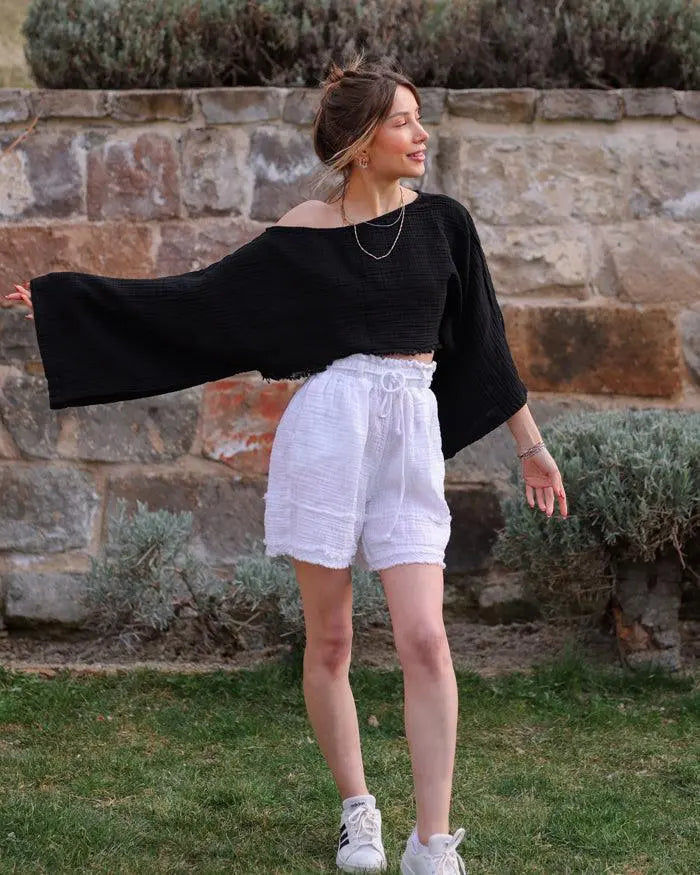 A close-up of white gauze shorts with a textured design, worn by a person also wearing a black top.