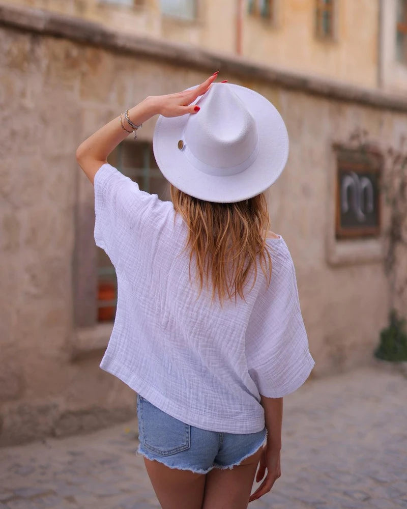 Woman wearing a white hat and white crinkle cotton tshirt with denim shorts in an outdoor setting.