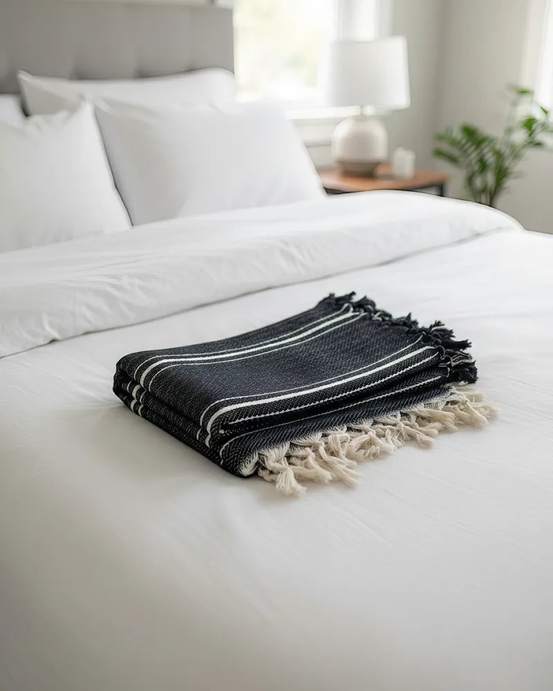 Black and white striped cotton throw blanket with tassels folded on a white bed