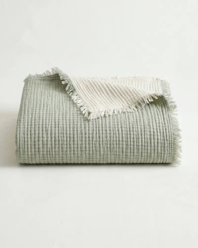 Sage green muslin throw blanket folded with frayed edges