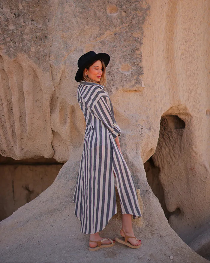 Woman in a striped maxi shirt dress and black hat standing in front of stone walls.