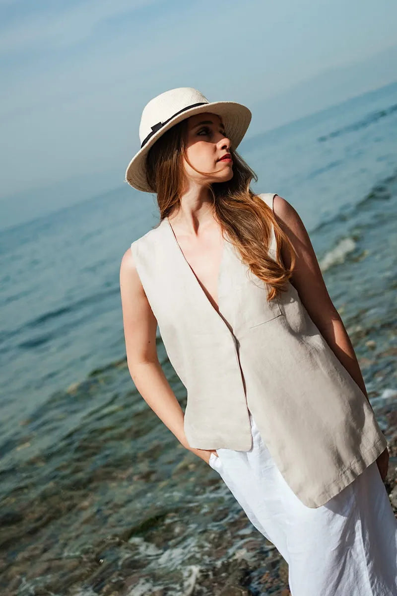 Woman wearing a beige sleeveless top and white hat by the water