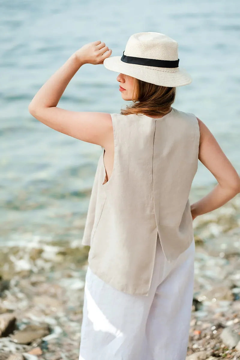 Woman wearing a beige linen vest and white pants on a beach.