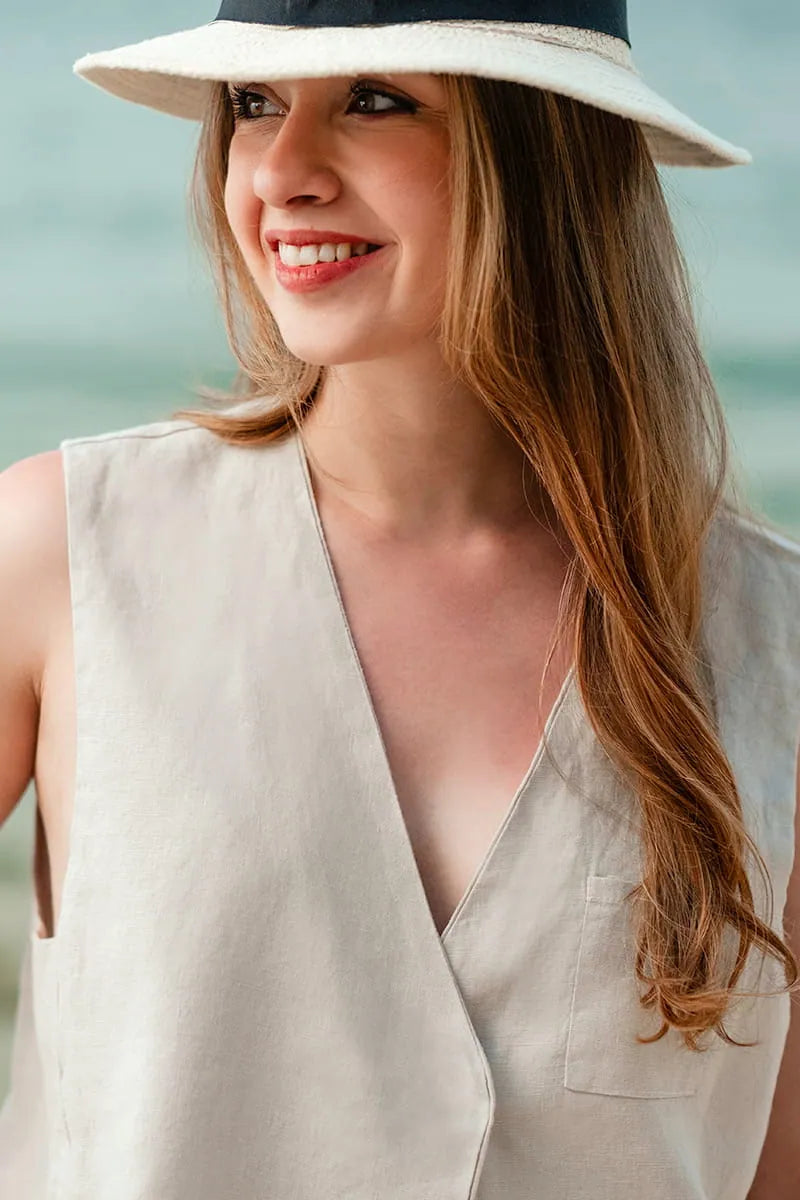 Woman wearing a beige sleeveless vest top and a wide-brimmed hat with a blurred background