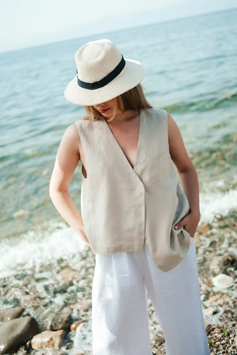 Woman wearing a beige sleeveless vest and white linen pants on a beach.