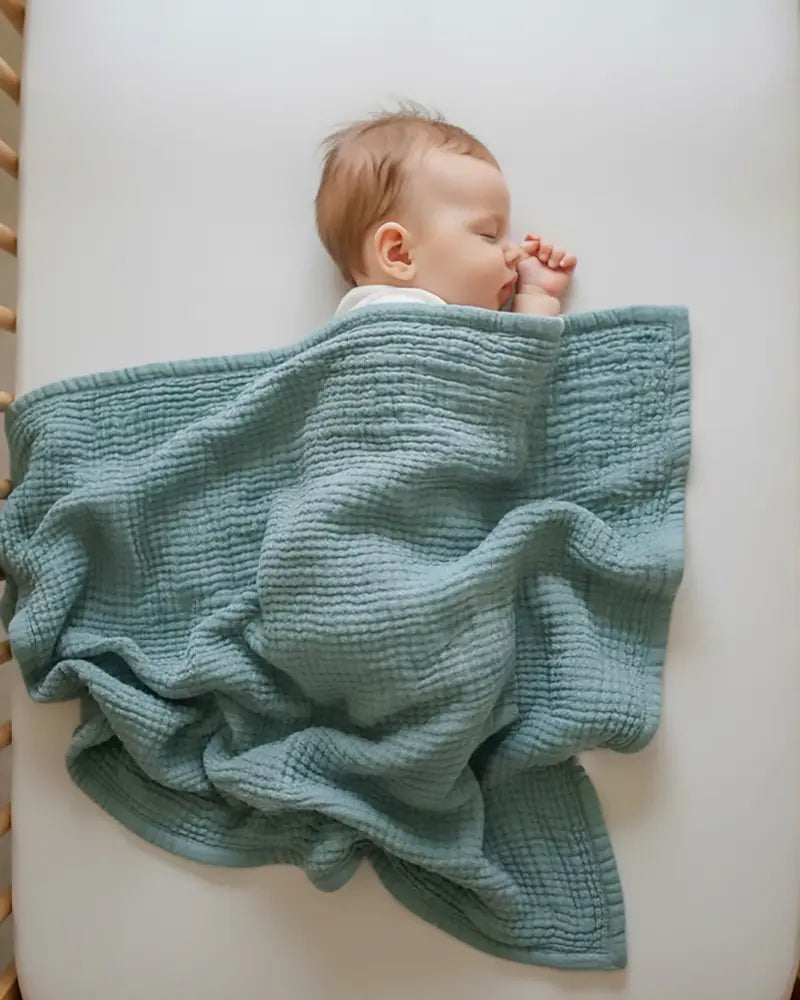Baby wrapped in a light blue blanket on a white surface