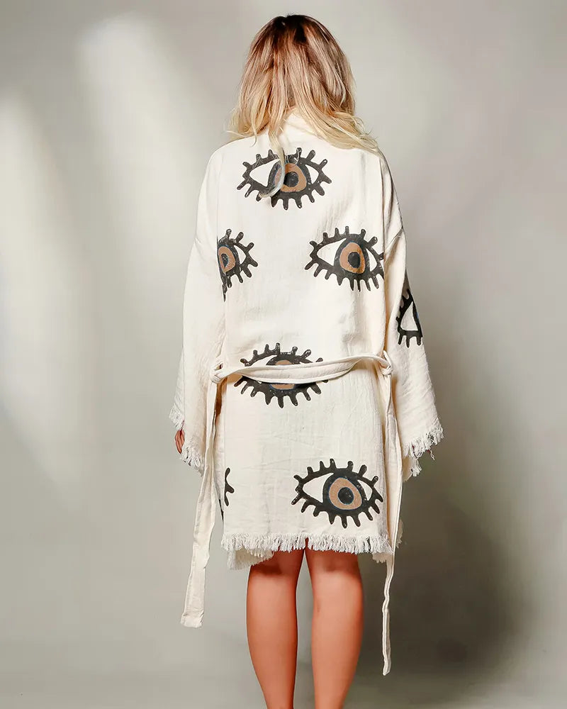 Woman wearing a white kimono-style garment with eye patterns on a plain background