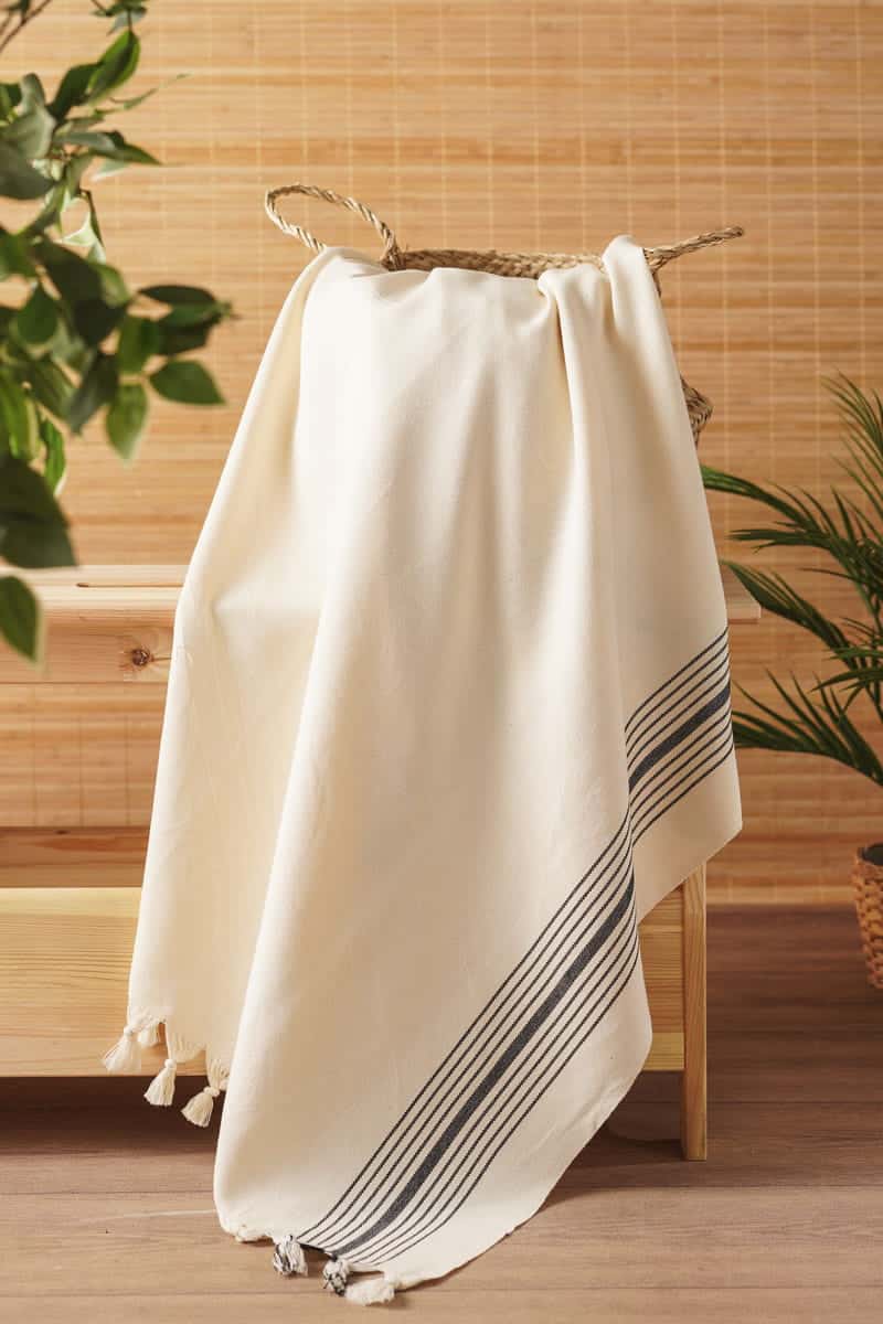 white towel with black stripes hanging on a wooden rack with plants in the background