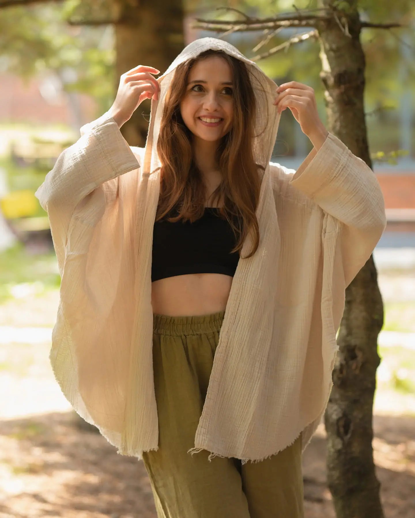 Woman wearing a beige Hoodie cardigan over a black top and green pants in a park setting