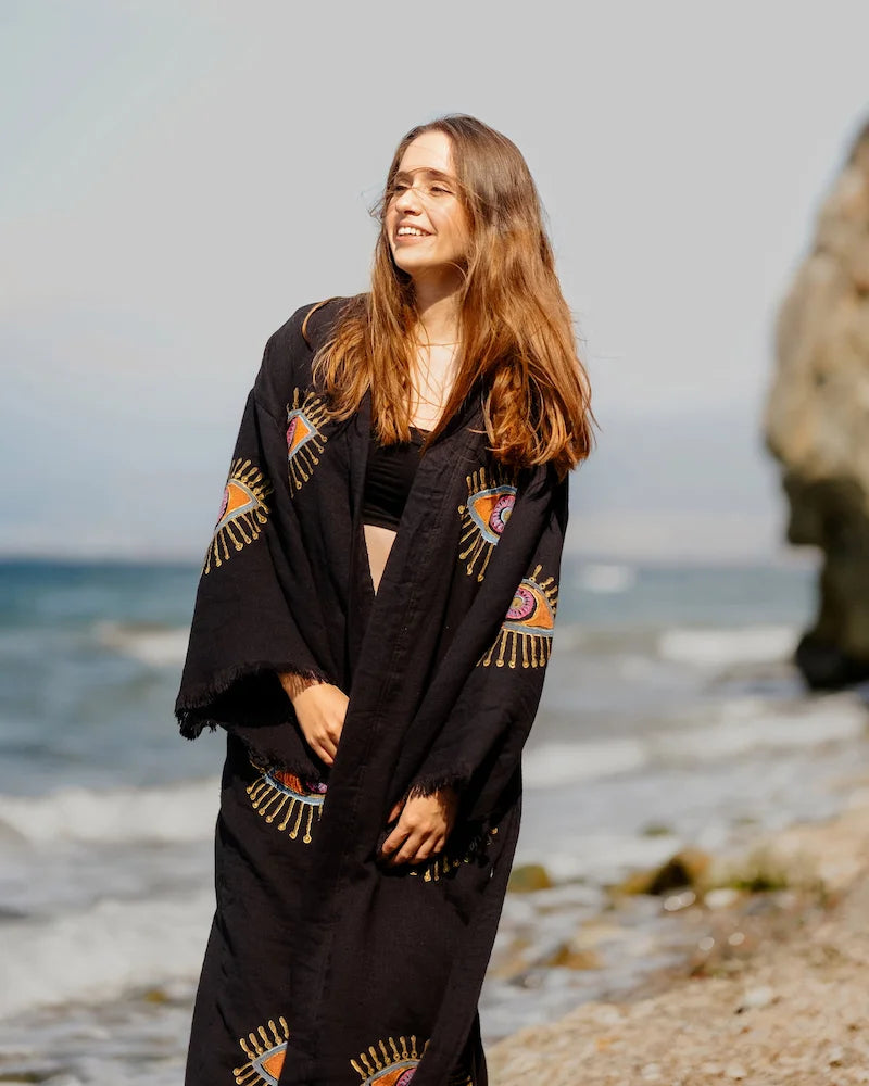 Woman wearing a black evil eye robe with geometric patterns on a beach