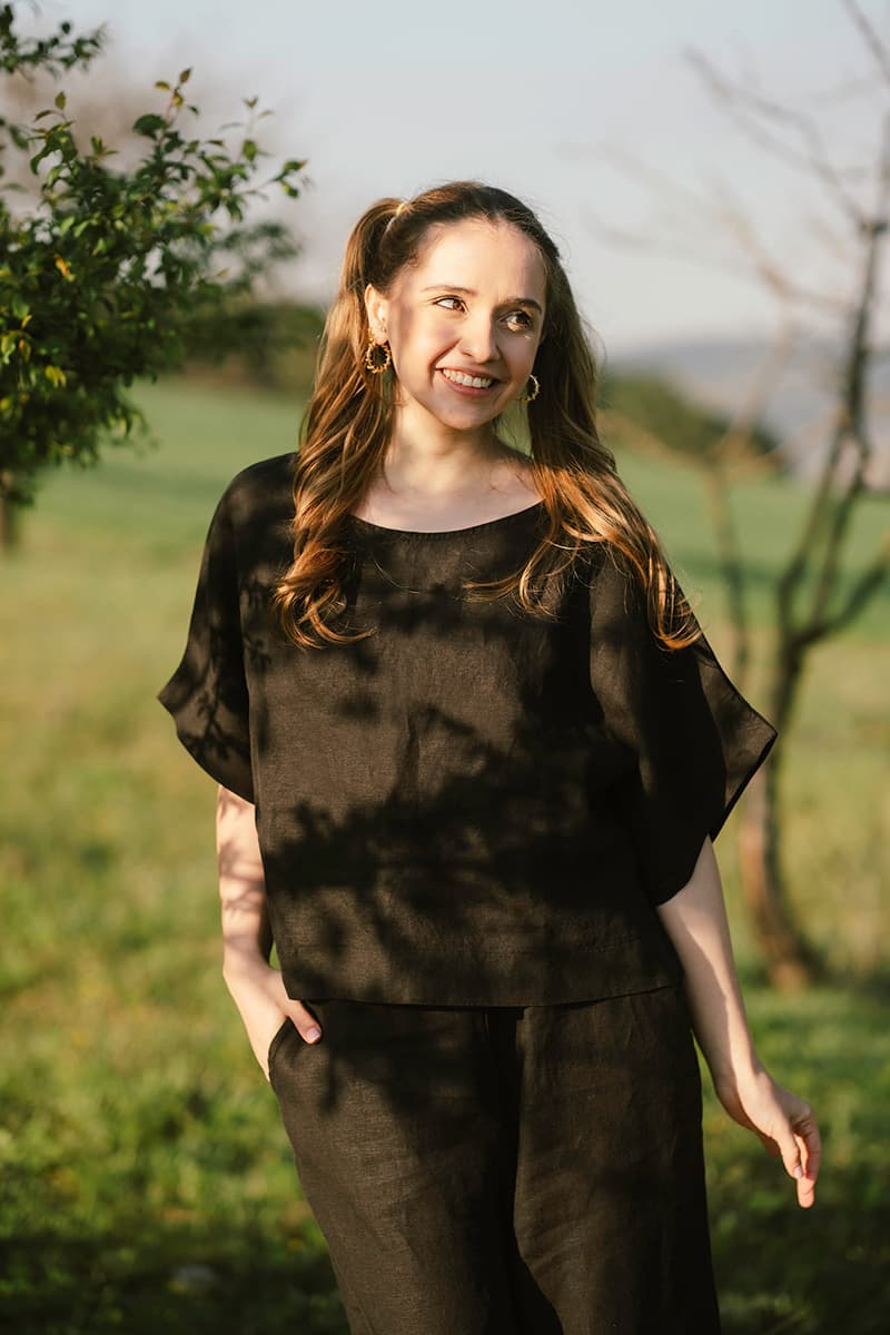 Woman standing outdoors in a field wearing a Black Linen Top.