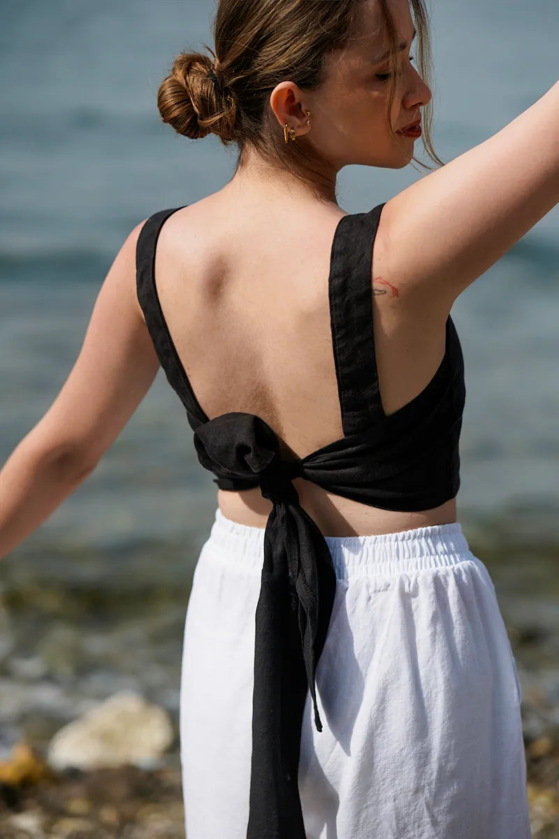 Woman wearing a black tie back crop top and white pants by a body of water