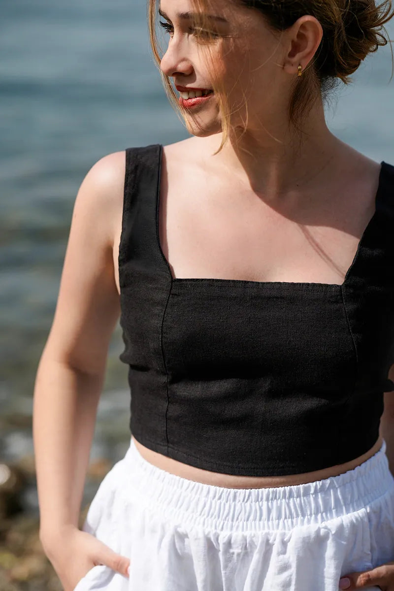 Woman wearing a black crop top and white pants by a body of water
