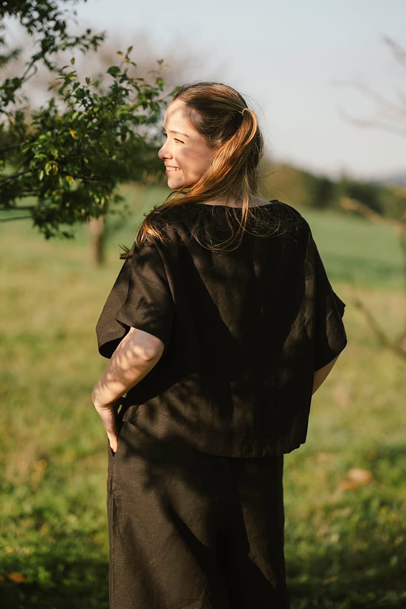 Woman in a black blouse standing in a field with trees and grass in the background