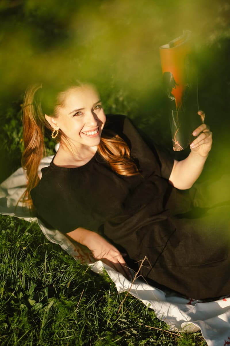 A woman reclines on a blanket in a black linen t-shirt and white palazzo pants, holding a vibrant kite in a grassy space.