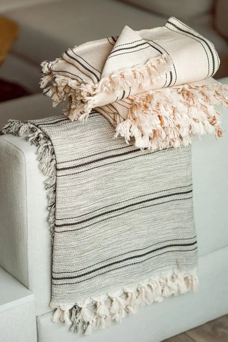 handwoven cotton grey throw blanket with tassels draped over a white armchair.