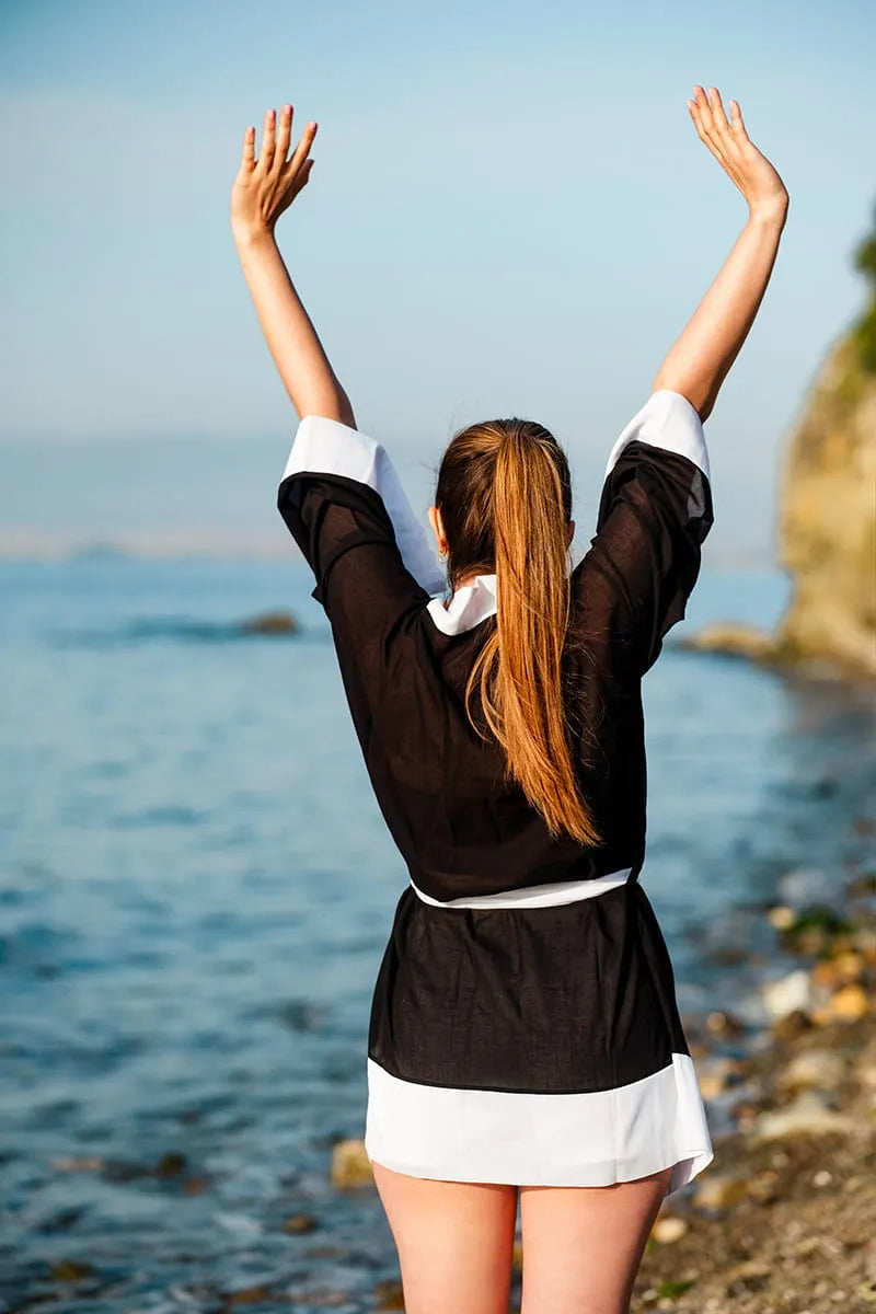 Woman with beach coverp arms raised by the ocean