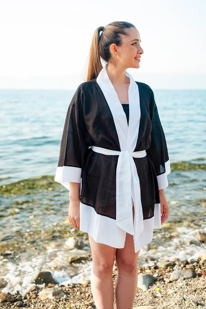 Woman wearing a black and white robe standing on a beach.