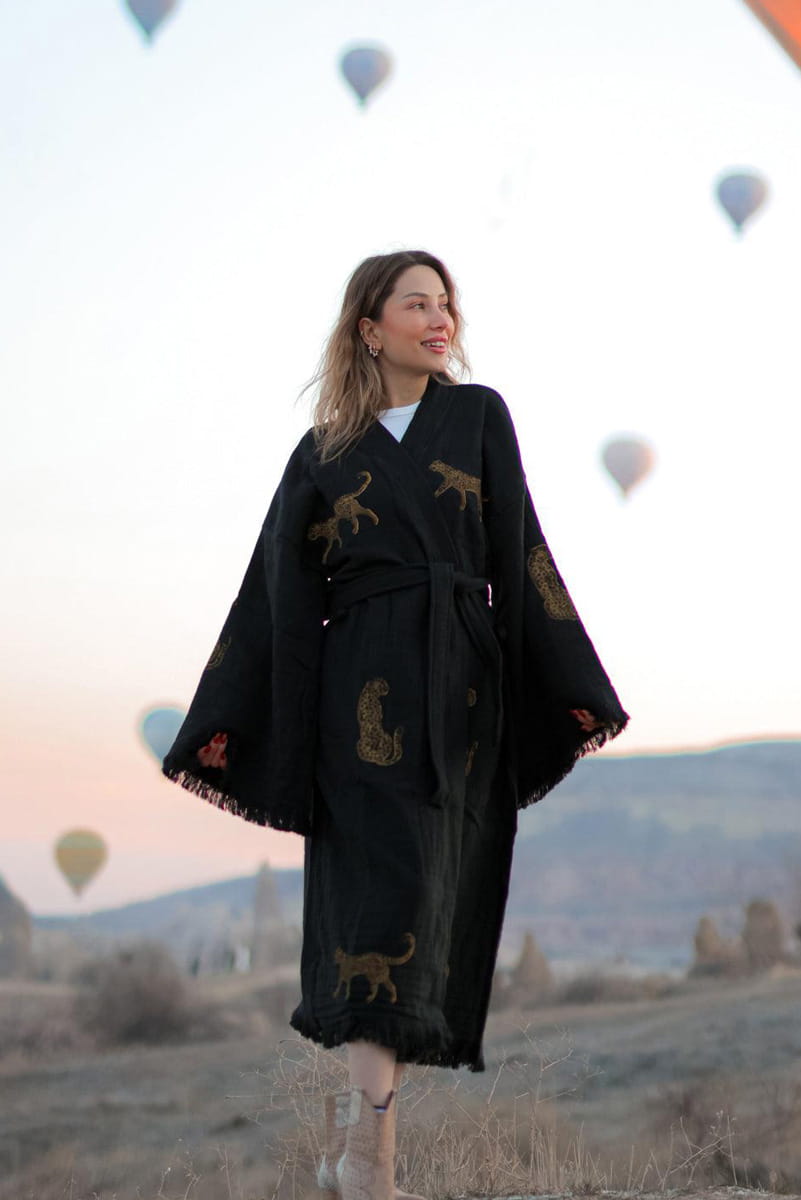 Woman wearing a black outfit with golden tiger print against a scenic background with hot air balloons.