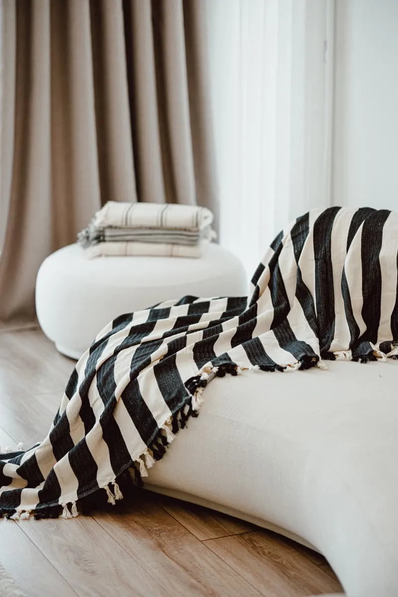 Black and white striped blanket draped over a white sofa with neutral curtains in the background.
