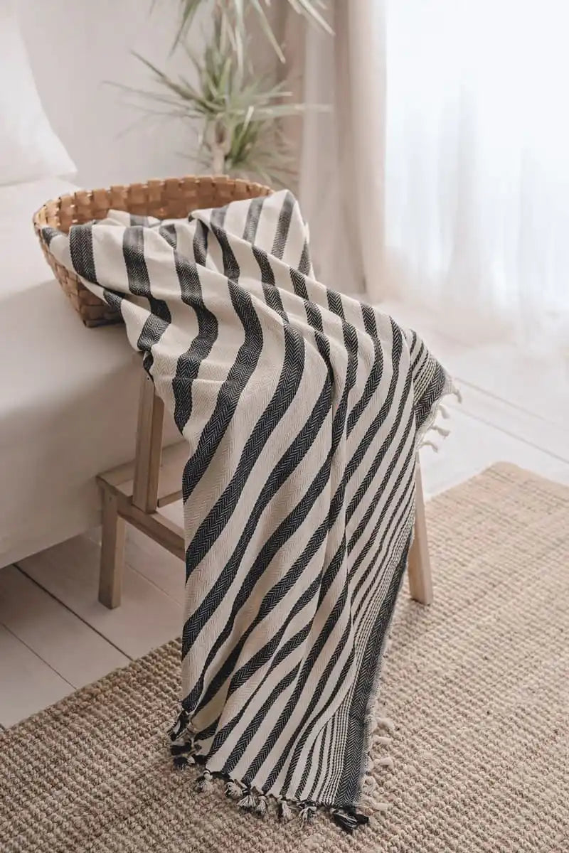 Striped blanket draped over a chair in a room with a plant and white curtain.