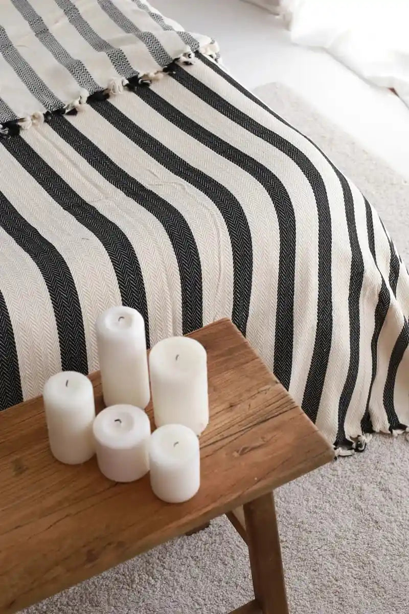 White candles on a wooden table with a black and white striped blanket in the background