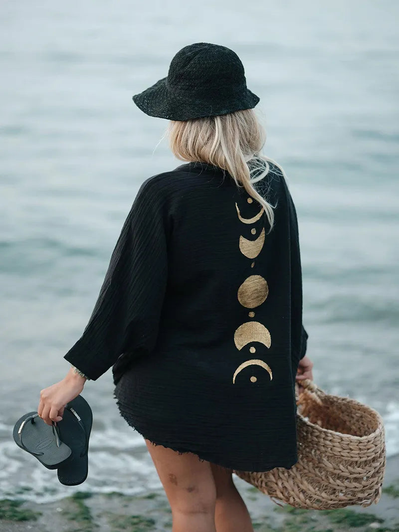 Person wearing a black cardigan with gold moon phases by a body of water