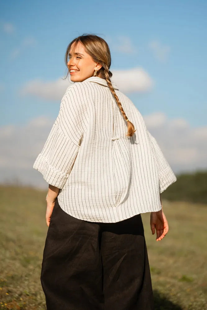 Woman standing with a striped shirt in a field with a blue sky and clouds in the background